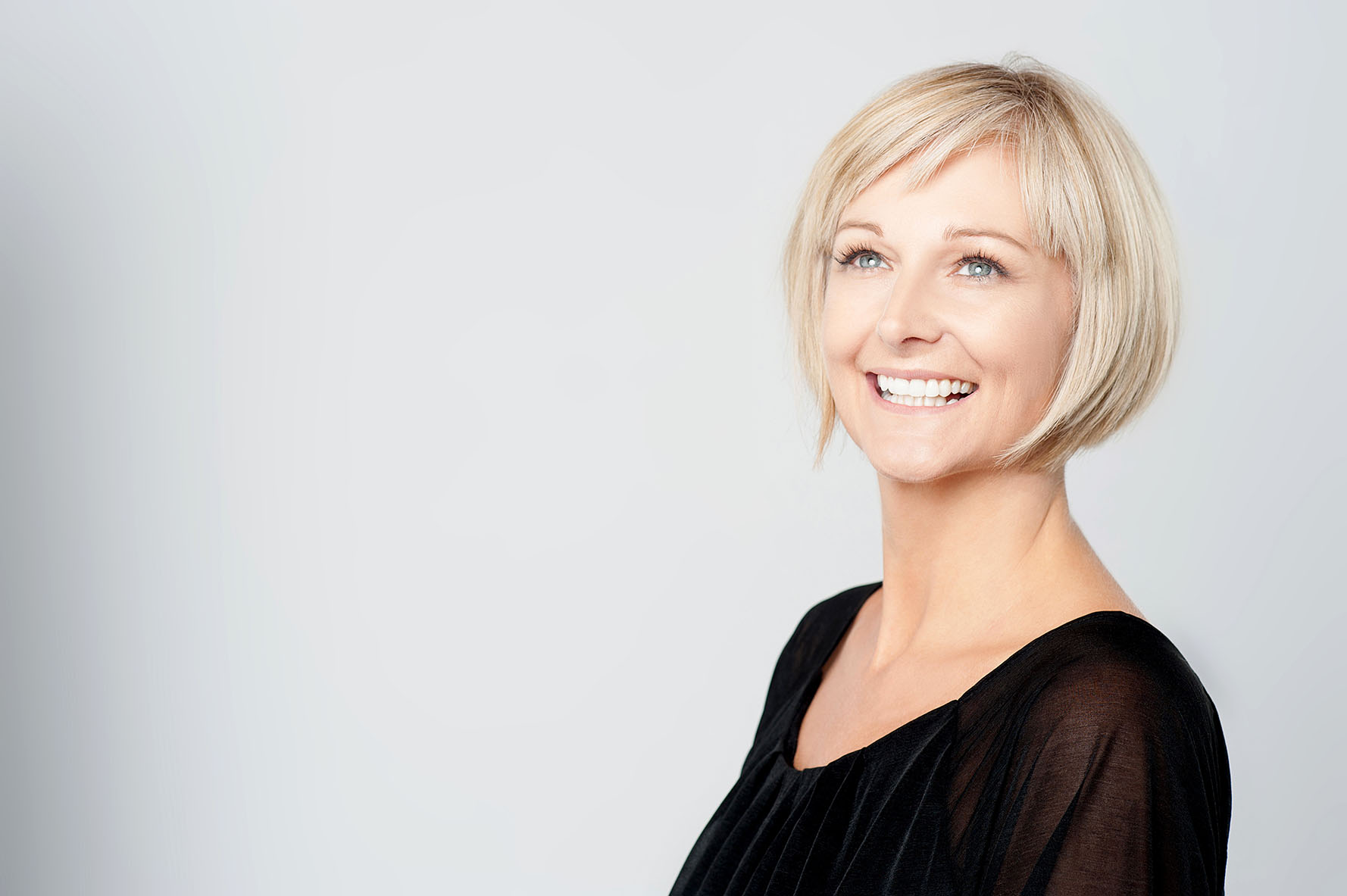 Woman with smooth, youthful skin smiling confidently and looking slightly upward.