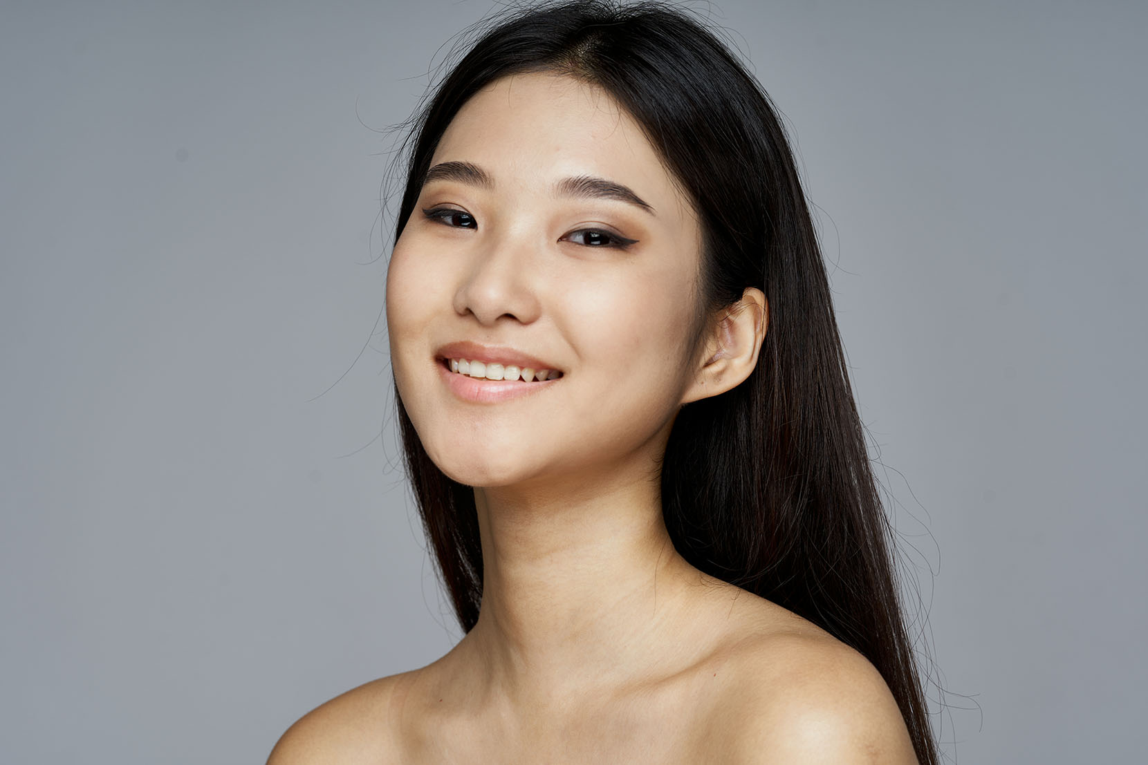 Woman smiling gently while looking slightly upward, with long dark hair and bare shoulders.