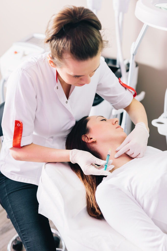 Practitioner wearing gloves holds a syringe near a woman’s neck while she lies on a treatment chair.