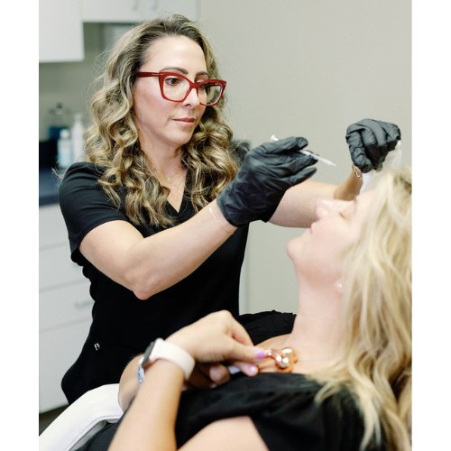 Aesthetic provider administering a Botox injection to a woman's lower face while she lies comfortably.